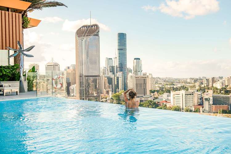 A stunning 23-meter rooftop infinity pool at Emporium Hotel South Bank at dusk, overlooking the Brisbane River and illuminated city skyline.