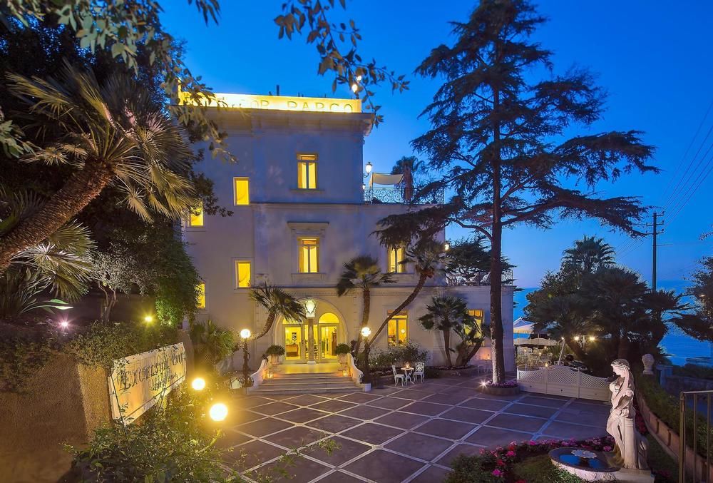 A sun-drenched private terrace at Luxury Villa Excelsior Parco featuring a white Jacuzzi, floral Art Nouveau tiles, and a sweeping view of the Bay of Naples.