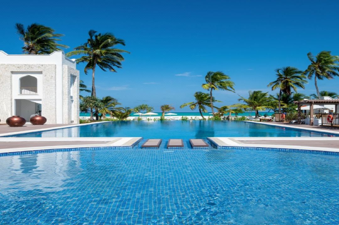 Infinity pool at LUX* Marijani Zanzibar merging with the turquoise Indian Ocean, framed by white Omani-style architecture.