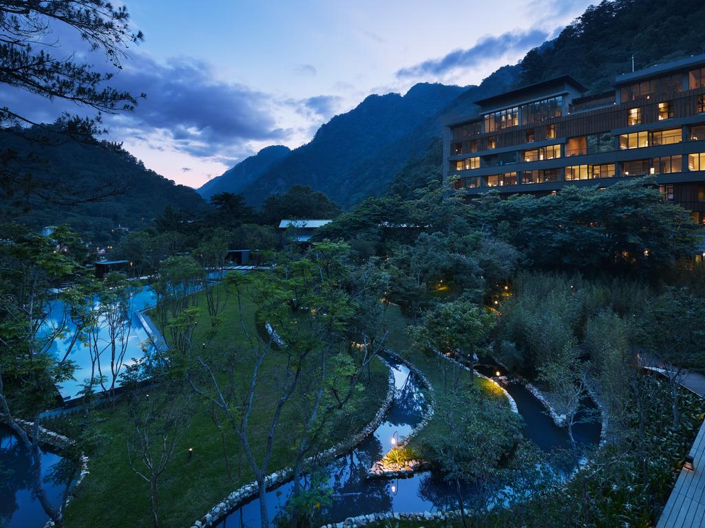 A guest relaxing in a private semi-open air onsen at HOSHINOYA Guguan, overlooking lush Taiwanese mountains through floor-to-ceiling glass.